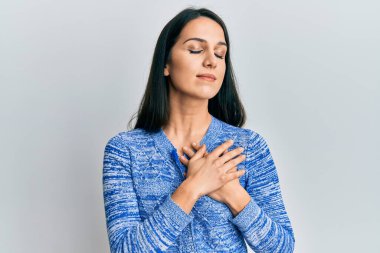 Gündelik kıyafetler giyen genç İspanyol kadın elleri göğsünde gülümsüyor, gözleri kapalı, yüzünde minnet ifadesi var. sağlık kavramı. 