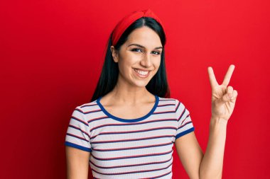 Gündelik kıyafetler giyen, gülümseyen, kameraya göz kırpan genç İspanyol kadın zafer işareti yapıyor. İki numara.. 