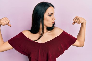 Sıradan kıyafetler giyen genç İspanyol kadın gururla gülümseyen kol kaslarını gösteriyor. fitness konsepti. 