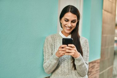 Genç İspanyol kadın şehirde akıllı telefon kullanarak mutlu bir şekilde gülümsüyor..