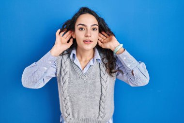 Mavi arka planda duran genç esmer kadın iki elini de kulak hareketlerinde, dedikoduya meraklı olarak duymaya çalışıyor. İşitme sorunu, sağır 