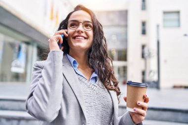 Genç İspanyol kadın yönetici kahve içiyor ve caddede akıllı telefondan konuşuyor.