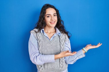 Mavi arka planda duran esmer kadın gülümseyerek doğal bir şekilde içeri girmeye davet ediyor. 