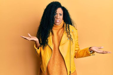 Orta yaşlı Afro-Amerikalı kadın yün kazak ve deri ceket giyiyor. Hiçbir şeyden habersiz ve kolları açık, hiçbir fikri yok.. 