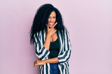 Orta yaşlı Afro-Amerikalı kadın günlük kıyafetler giyiyor kameraya bakıyor kollarını kavuşturup gülümsüyor ve çenesini kaldırıyor. Olumlu düşünmek. 