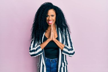 Orta yaşlı Afro-Amerikalı kadın gündelik giysiler giyip birlikte dua ederek af diliyor kendinden emin bir şekilde gülümseyerek.. 