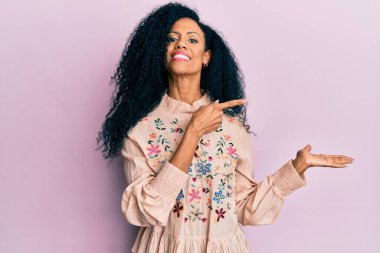 Orta yaşlı Afro-Amerikalı kadın gündelik giysiler giyip kameraya hayret ediyor ve gülümsüyor.. 