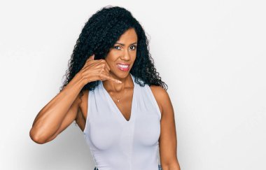 Orta yaşlı Afro-Amerikalı kadın, kolsuz tişörtsüz rahat giyiniyor, gülümsüyor, telefonla el ve parmak hareketleri yapıyor, telefonda konuşuyor gibi. iletişim kavramları. 