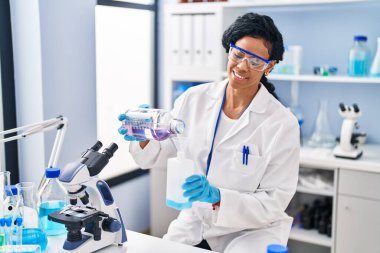 Laboratuvarda sıvı ölçen bilim adamı üniforması giyen Afrikalı Amerikalı kadın.