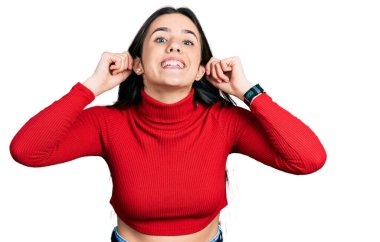 Kırmızı balıkçı yaka kazak giyen genç esmer kız, gülümsüyor kulakları parmaklarıyla çekiyor, komik bir jest. deneme sorunu 