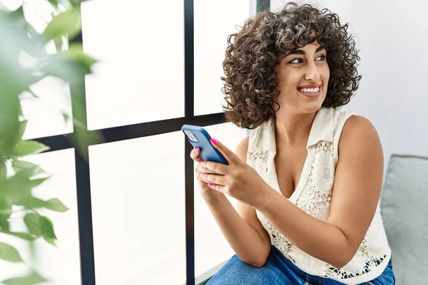 年轻的中东女人在家里用智能手机充满自信地微笑 — 图库照片