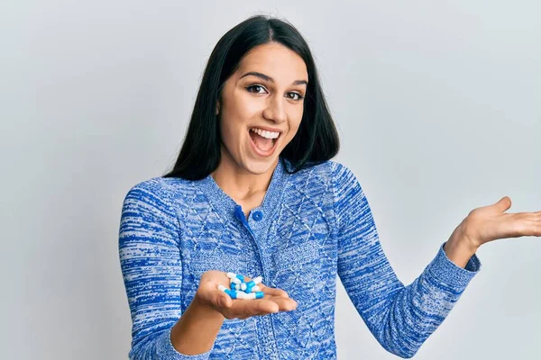 Genç İspanyol kadın elinde haplarla başarıyı kutluyor mutlu bir gülümsemeyle ve kazanan yüz ifadesiyle elini kaldırarak. 