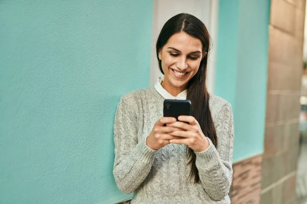 Genç İspanyol kadın şehirde akıllı telefon kullanarak mutlu bir şekilde gülümsüyor..