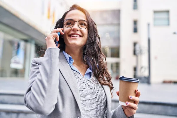 Genç İspanyol kadın yönetici kahve içiyor ve caddede akıllı telefondan konuşuyor.