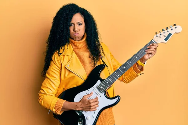 Orta yaşlı Afro-Amerikalı bir kadın komik suratlı, elektro gitar şişirme yanakları oynuyor. Ağzı havayla şişer, havayı yakalar.. 