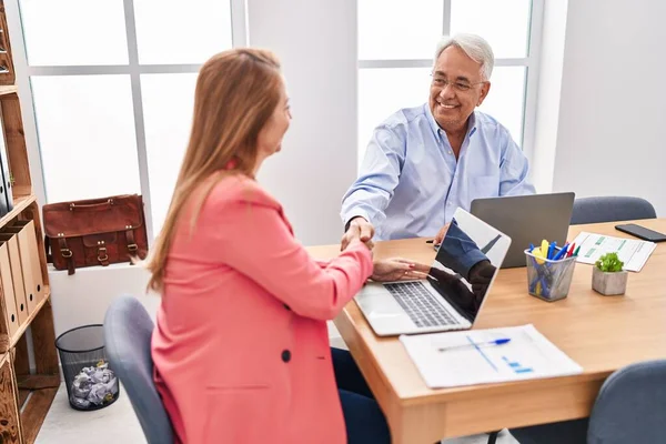 Orta yaşlı erkek ve kadın iş adamları ofiste el sıkışıyor.
