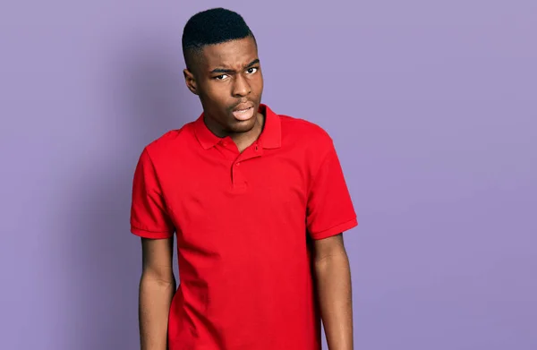 衝撃の顔にカジュアルな赤いTシャツを着て若いアフリカ系アメリカ人の男 懐疑的で皮肉を探して オープン口で驚いて — ストック写真