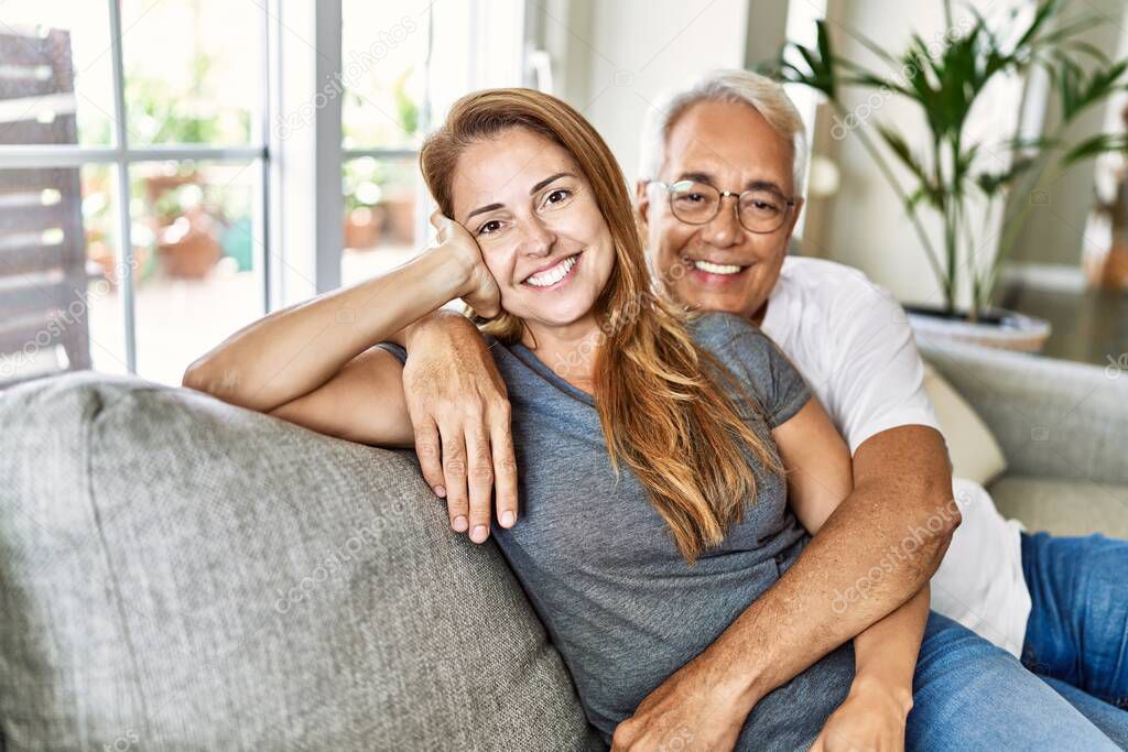 Middle age hispanic couple smiling happy and hugging sitting on the sofa at home.