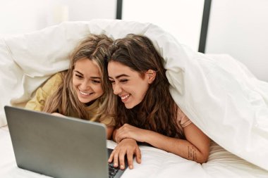 Yatakta çarşafla film izleyen genç çift..