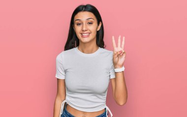 Gündelik beyaz tişört giyen genç İspanyol kız üç numarayı gösterip işaret ederken kendinden emin ve mutlu gülümsüyor.. 