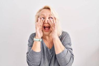 Beyaz arka planda duran orta yaşlı beyaz kadın elleri ağızda bağırarak bağırıyor. 