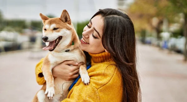 Güzel genç bir kadın sokakta mutlu Shiba Inu köpeğine sarılıyor.