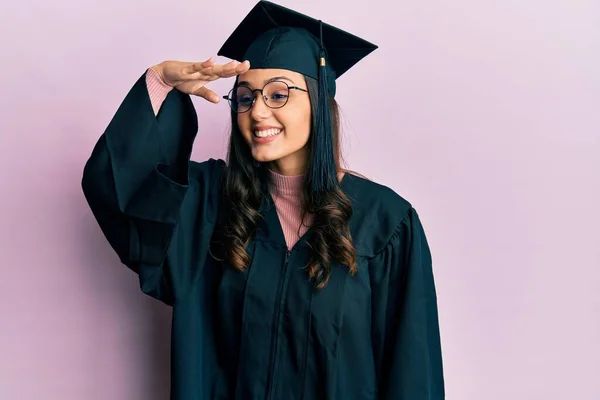 卒業キャップと式のローブを身に着けている若いヒスパニック系の女性は非常に幸せと笑顔遠くに手を頭の上に見て 検索の概念 — ストック写真