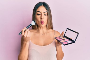 Makyaj fırçası tutan ve yüzü kızaran genç İspanyol kadın. Ağzı ve şaşı gözleriyle balık suratı yapıyor. Deli ve komik.. 