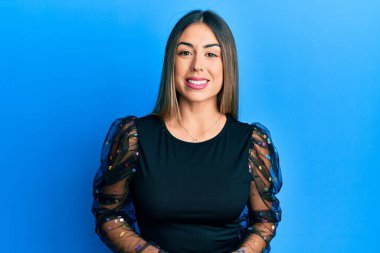 Gündelik kıyafetler giyen genç İspanyol kadın pozitif ve mutlu görünüyor. Dişlerini gösteren kendine güvenen bir gülümsemeyle ayakta ve gülümsüyor. 