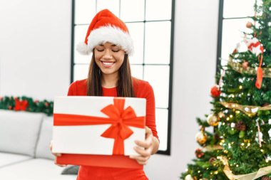 Genç Latin kadın boks hediyesini açıyor. Noel ağacının yanında duruyor.