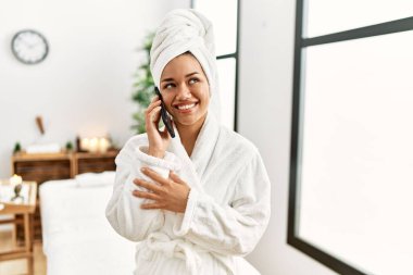 Bornoz giyen genç Latin kadın güzellik merkezinde kredi kartı tutuyor.