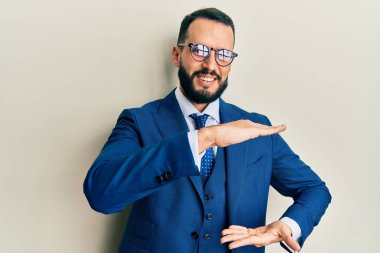 Sakallı, takım elbiseli ve kravatlı, elleri büyük ve büyük boy işareti olan genç bir adam. Ölçü sembolü. Kameraya bakıp gülümsüyor. ölçüm kavramı. 