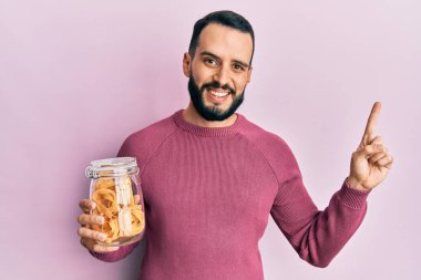 Sakallı genç adam elinde makarna kavanozuyla gülümsüyor. 