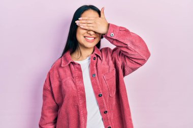 Güzel İspanyol bir kadın, burun piercingli, sıradan pembe bir ceket giyiyor, gülümsüyor ve elleri yüzünde, şaşırtmak için gözlerini kapatıyor. kör kavram. 