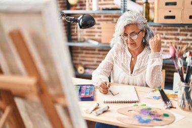 Sanat stüdyosunda not defterine çizim yapan orta yaşlı kadın sanatçı.