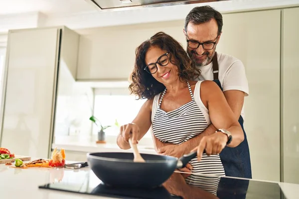 Orta yaşlı İspanyol çift gülümsüyor. Kendilerine güveniyorlar ve mutfakta yemek pişiriyorlar.