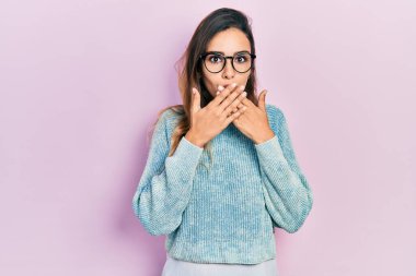 Günlük kıyafet ve gözlük takan genç İspanyol kız yanlışlıkla elleri ile ağzını kapatırken şok oldu. gizli kavram. 