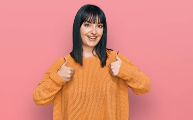 Gündelik kıyafetler giyen genç İspanyol kadın. Başarı işareti ile el hareketi yapıyor. Gülümsüyor ve mutlu. Neşeli ifade ve kazanan jest. 