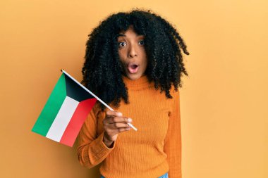 Afro saçlı, kuveyt bayrağı tutan Afro-Amerikalı bir kadın ağzı açık kalmış, korkmuş ve şaşırmış bir şekilde şaşırmış, inançsız bir yüz ifadesi var. 