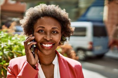 Güzel iş kadını afro saçlı Afro-Amerikan kadın mutlu ve kendinden emin bir şekilde şehirde telefonda konuşuyor.