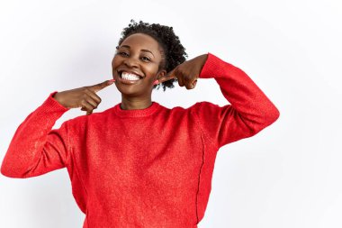 Genç Afro-Amerikalı kadın izole edilmiş arka planda günlük giysiler giyip neşeli gülüyor ve parmaklarıyla ve ağzıyla işaret ediyor. diş sağlığı kavramı. 