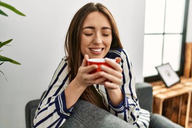 Genç İspanyol kadın evdeki kanepede kahve içiyor.