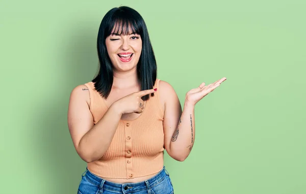 Young Hispanic Size Woman Pointing Open Palm Finger Winking Looking — Stockfoto