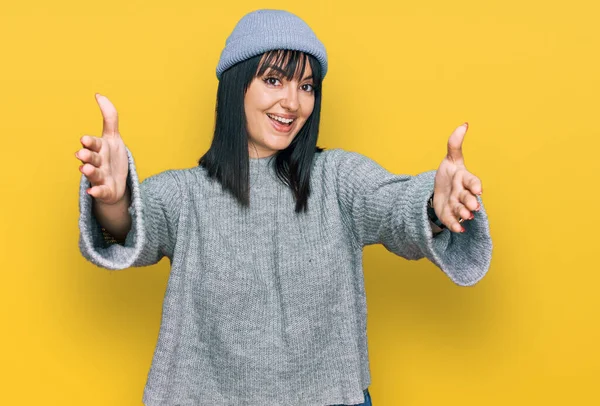 Şirin yün şapkalı genç İspanyol kadın kucaklanmak için kollarını açmış kameraya bakıyor. Mutluluğu kucaklayan neşeli bir ifade.. 