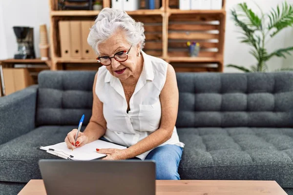 Psikoloji merkezinde dizüstü bilgisayar kullanarak panoya yazı yazan kıdemli gri saçlı kadın psikolog.
