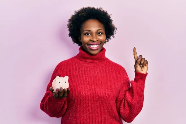 若いアフリカ系アメリカ人の女性は 幸せな顔をしたアイデアや質問を指差す指で笑顔で貯金箱を保持し ナンバーワン — ストック写真