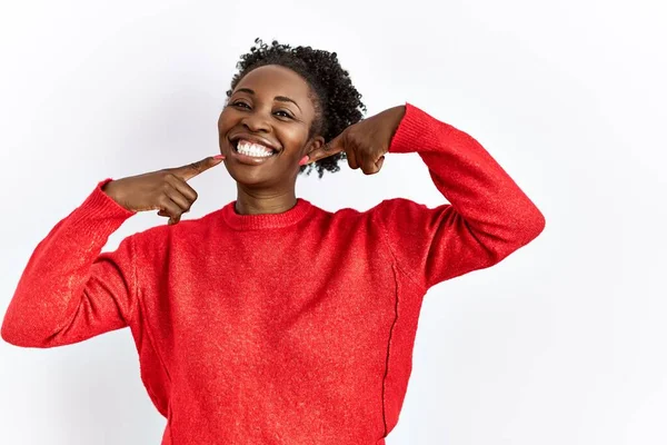 Genç Afro-Amerikalı kadın izole edilmiş arka planda günlük giysiler giyip neşeli gülüyor ve parmaklarıyla ve ağzıyla işaret ediyor. diş sağlığı kavramı. 