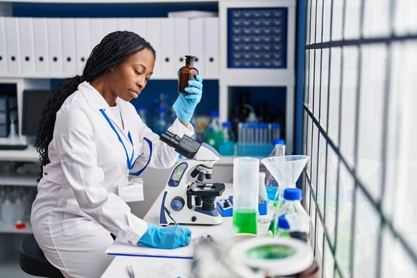 アフリカ系アメリカ人女性科学者の制服を着てクリップボード上の書き込みボトル研究室 — ストック写真