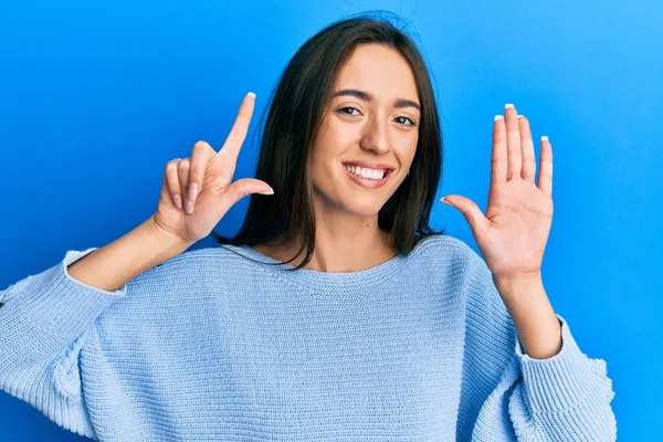 Gündelik kıyafetler giyen genç İspanyol kız yedinci parmaklarını gösterip işaret ederken kendinden emin ve mutlu bir şekilde gülümsüyor.. 