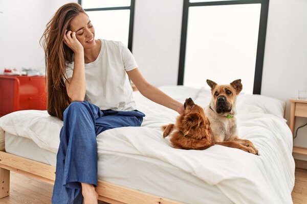 Young hispanic woman smiling confident sitting with dogs on bed at bedroom